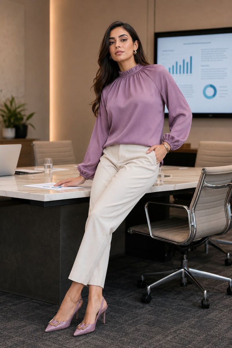 Woman in a purple blouse and white pants sitting at a conference table in an office setting.